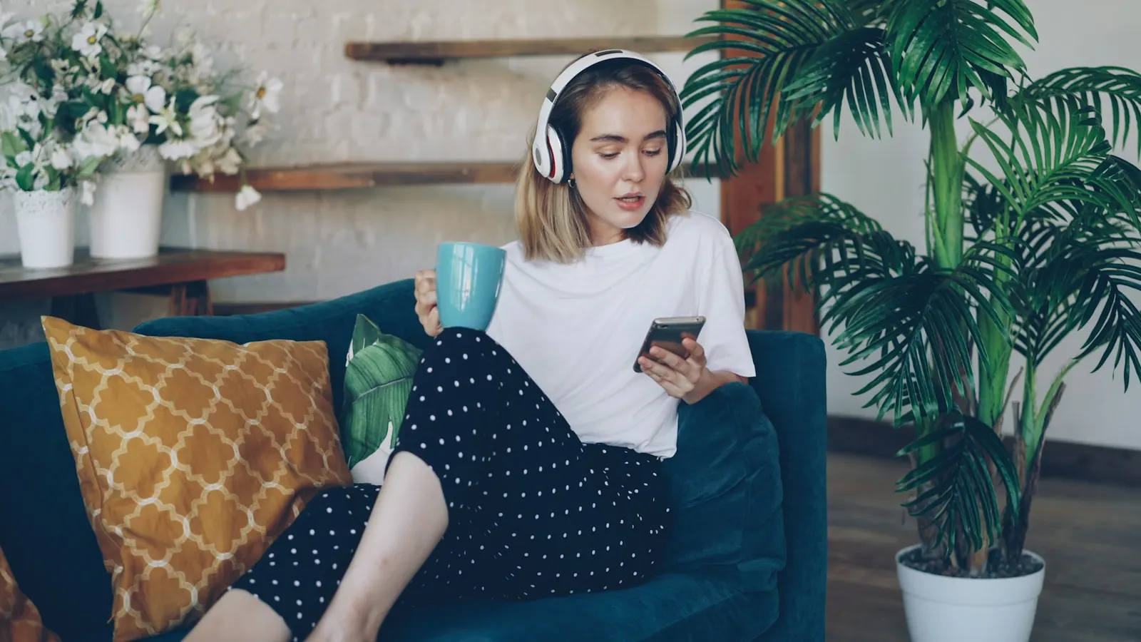 Frau mit Kopfhörern und Handy entspannt auf dem Sofa