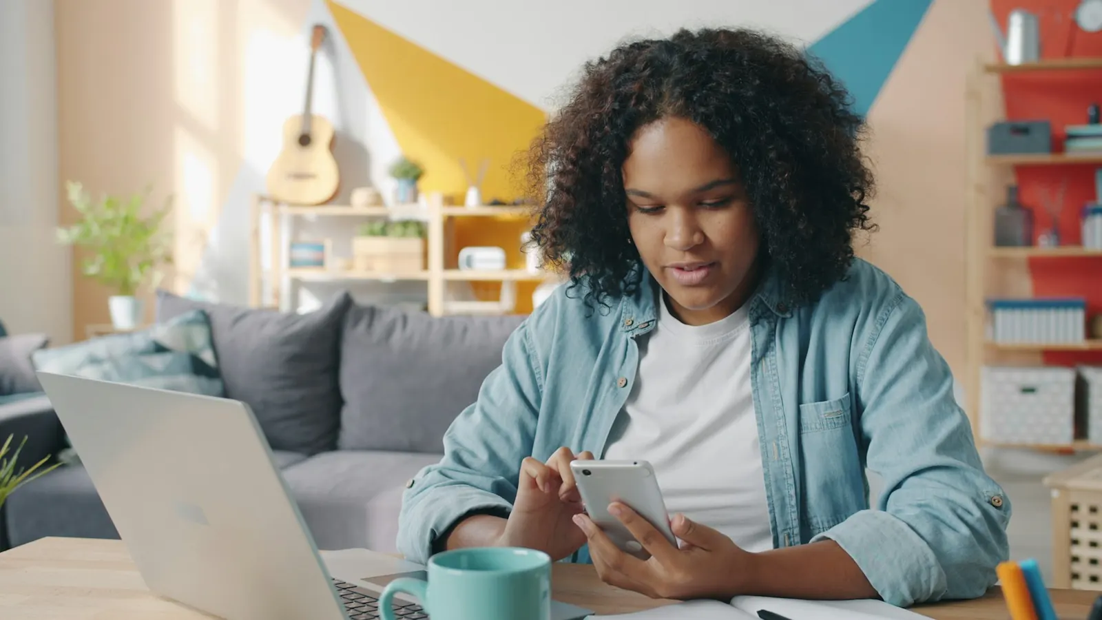 Junge Frau mit Handy und Laptop am Schreibtisch
